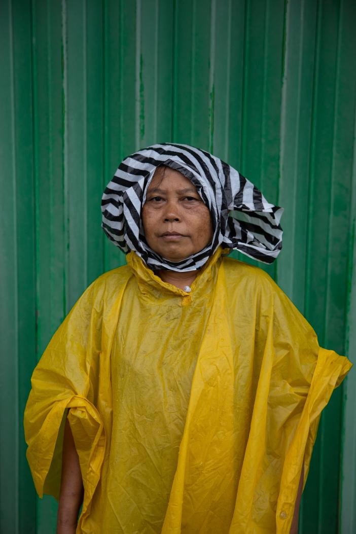 Portrait of a woman in a yellow raincoat with a striped plastic bag over her head, Gobleg, Bali