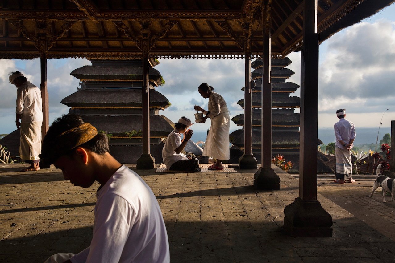 Worshippers in white move through the open pavilions of Besakih temple at dusk, Bali